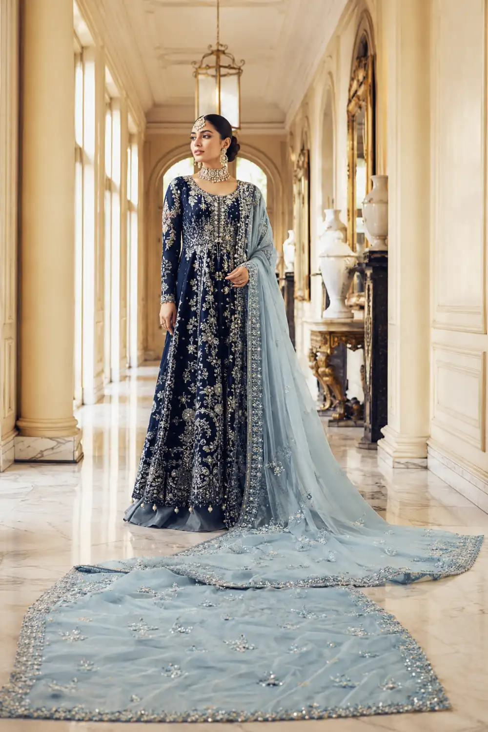 Midnight sapphire blue Pakistani couture gown featuring silver embroidery, crystal embellishments, floral motifs, and a dramatic ice-blue embellished dupatta. Full-length luxury formal dress designed for wedding receptions, engagement parties, festive occasions, and premium Pakistani fashion styling.