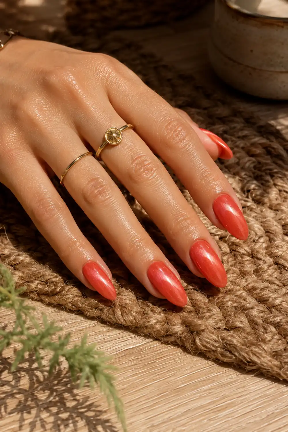 Coral glow cat eye nails with luminous magnetic shimmer on almond-shaped nails, displayed on a feminine hand resting on a woven rug over a wooden table in natural sunlight.