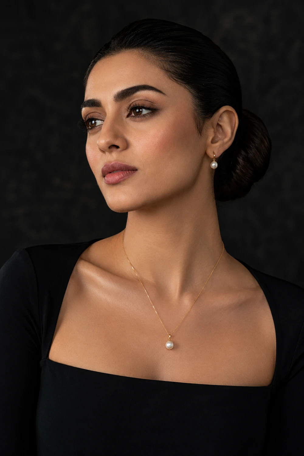 Woman wearing a minimalist pearl drop pendant necklace with a single freshwater pearl on a fine gold chain styled with a sophisticated black dress.