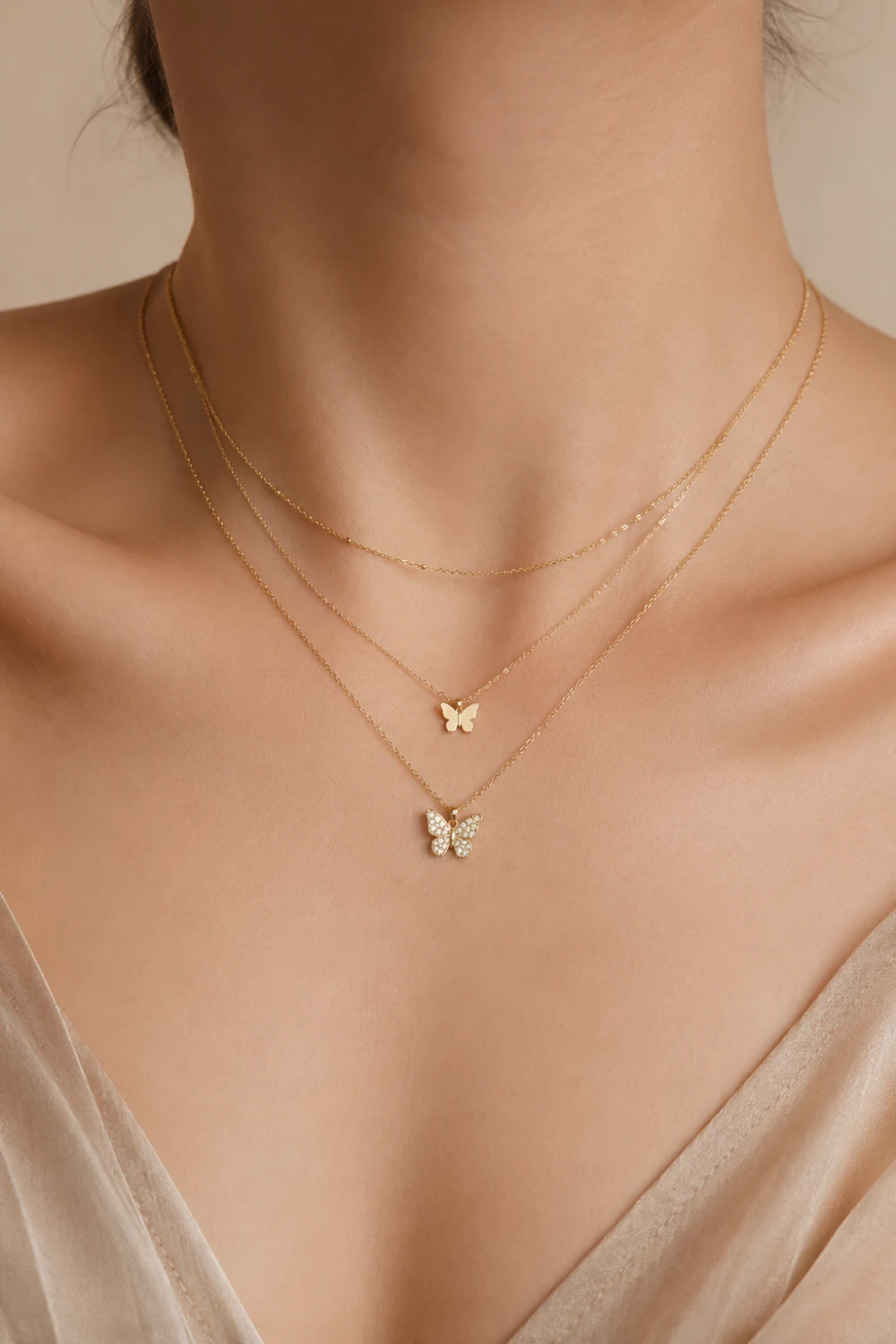 Woman wearing butterfly layered necklaces with delicate butterfly charms and gold chains styled with a neutral satin outfit.